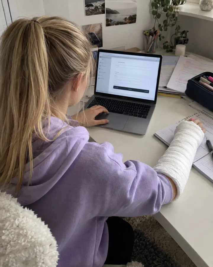 Jugendliche mit eingegipstem Unterarm bedient ein Formular am Laptop mit der anderen Hand