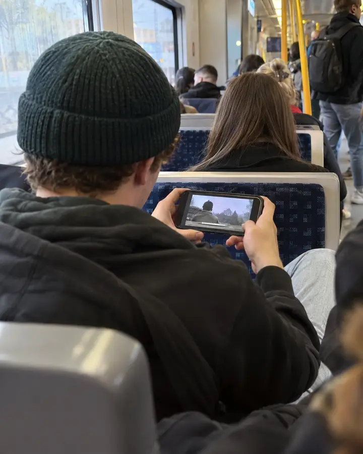 Junger Mann mit Mütze schaut in einer vollen Bahn ein Video auf dem Handy