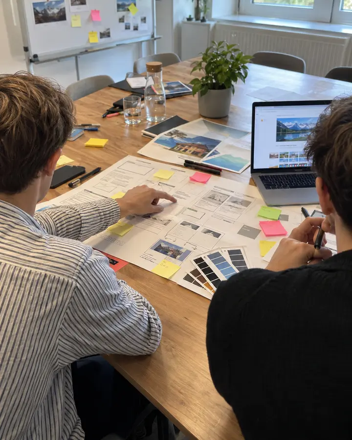 Zwei Menschen planen eine neue Website an einem Tisch mit ausgedrucktem Seitenplan, Klebezetteln und Farbmustern