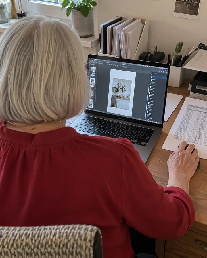 Frau bearbeitet ein PDF im Layoutprogramm, daneben liegt die ausgedruckte Preisliste